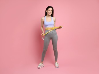 Photo of Happy young woman with measuring tape showing her slim body on pink background