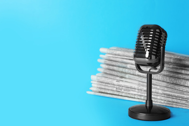 Photo of Newspapers and vintage microphone on light blue background, space for text. Journalist's work