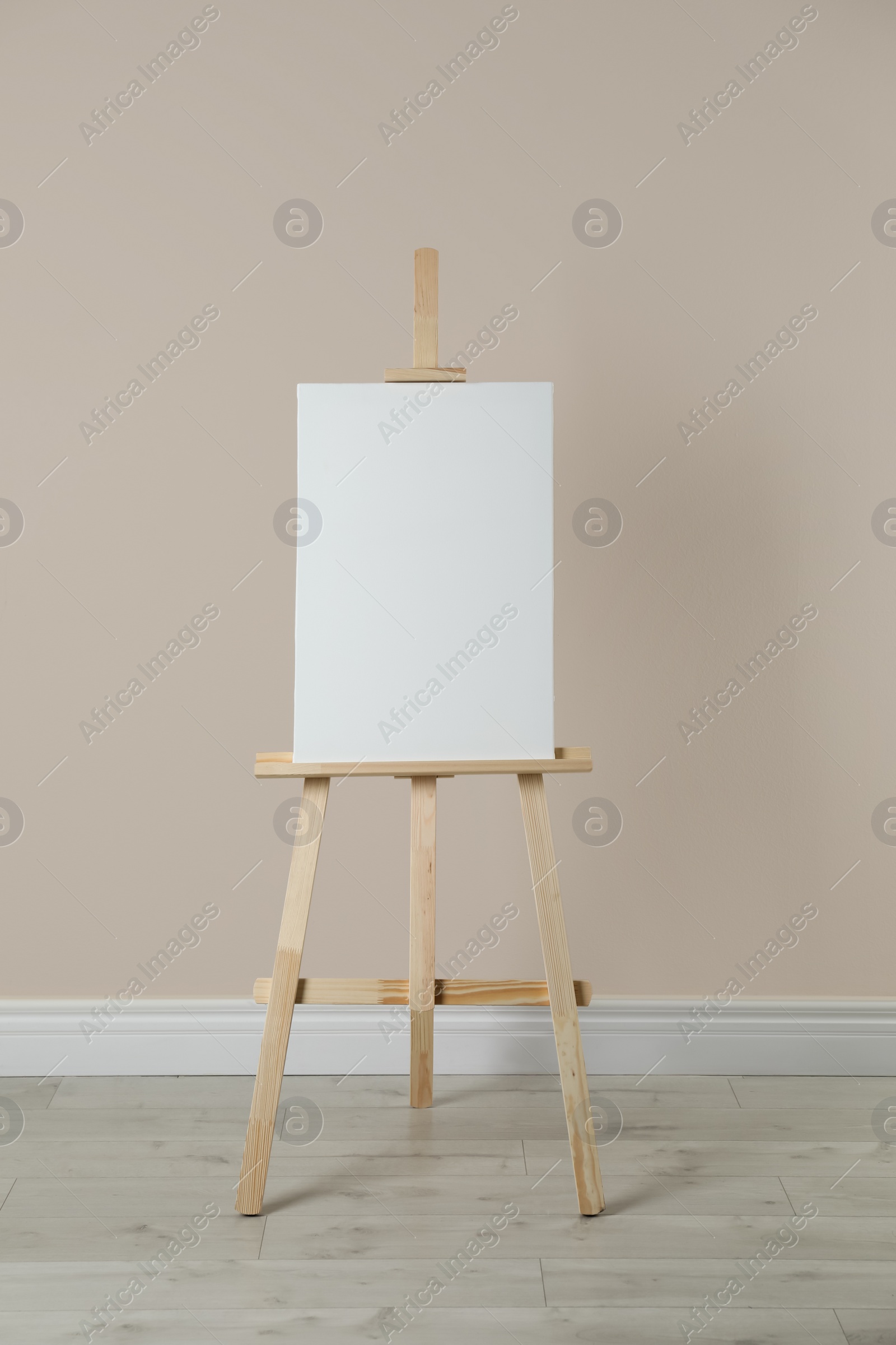 Photo of Wooden easel with blank canvas near beige wall