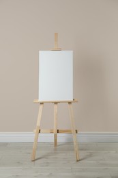 Photo of Wooden easel with blank canvas near beige wall