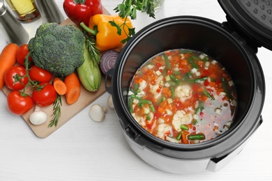 Modern multi cooker and products on white wooden table, above view