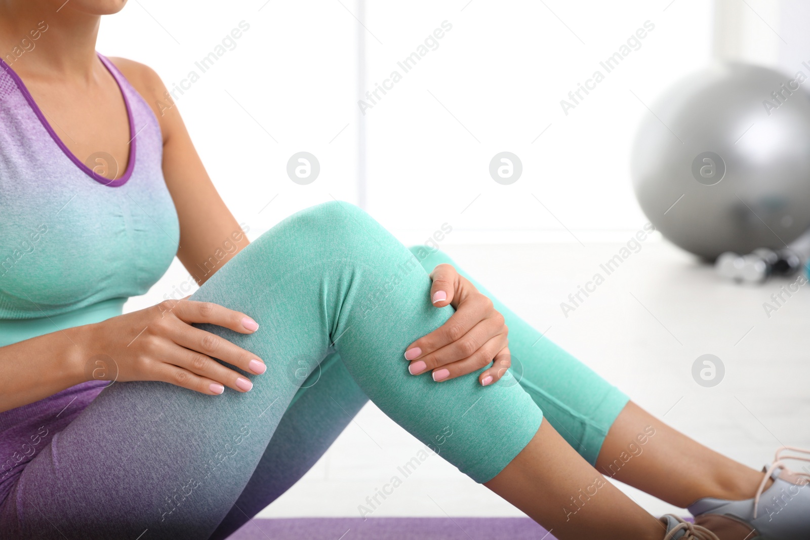 Photo of Young woman in sportswear having knee problems at gym, closeup. Space for text