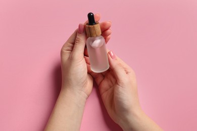 Photo of Woman holding bottle with serum on pink background, top view