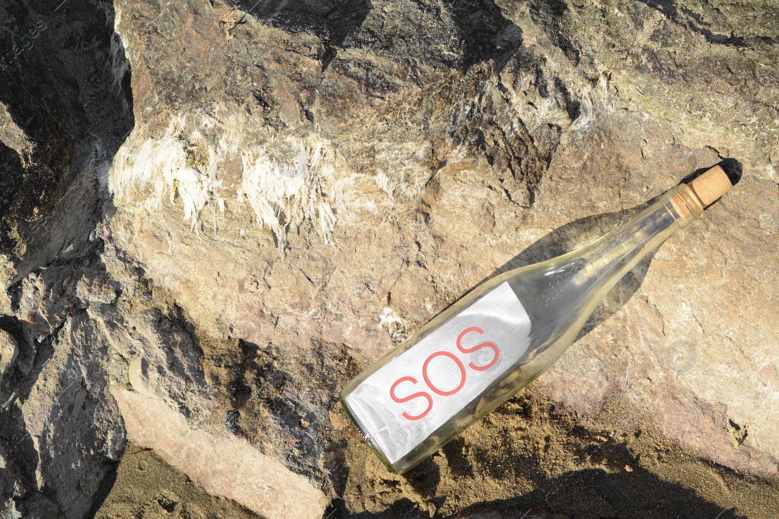 Photo of Glass bottle with SOS message on sea rock, top view