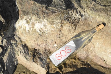 Photo of Glass bottle with SOS message on sea rock, top view