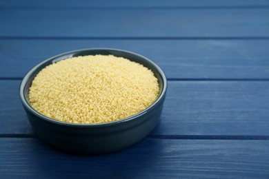 Bowl of raw couscous on blue wooden table, closeup. Space for text