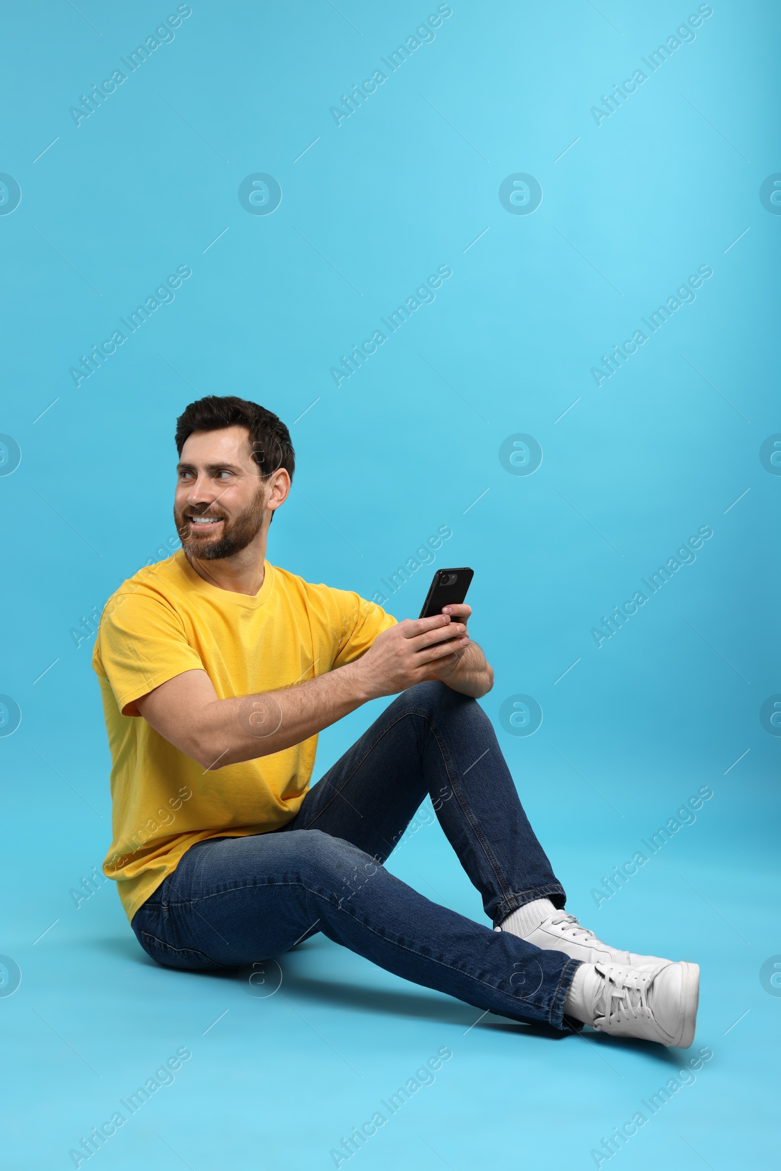 Photo of Smiling man with smartphone on light blue background