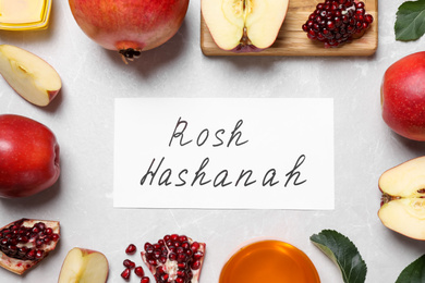 Photo of Card with text ROSH HASHANAH, apples, honey and pomegranates on white table, flat lay