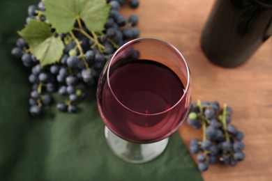 Photo of Glass of red wine and grapes on wooden table, above view
