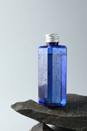 Photo of Bottle of cosmetic product on stone against light grey background, space for text