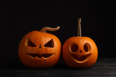 Scary jack o'lanterns made of pumpkins on wooden table against black background. Halloween traditional decor