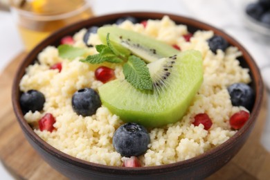 Photo of Bowl of tasty couscous with kiwi, blueberries and pomegranate on table, closeup