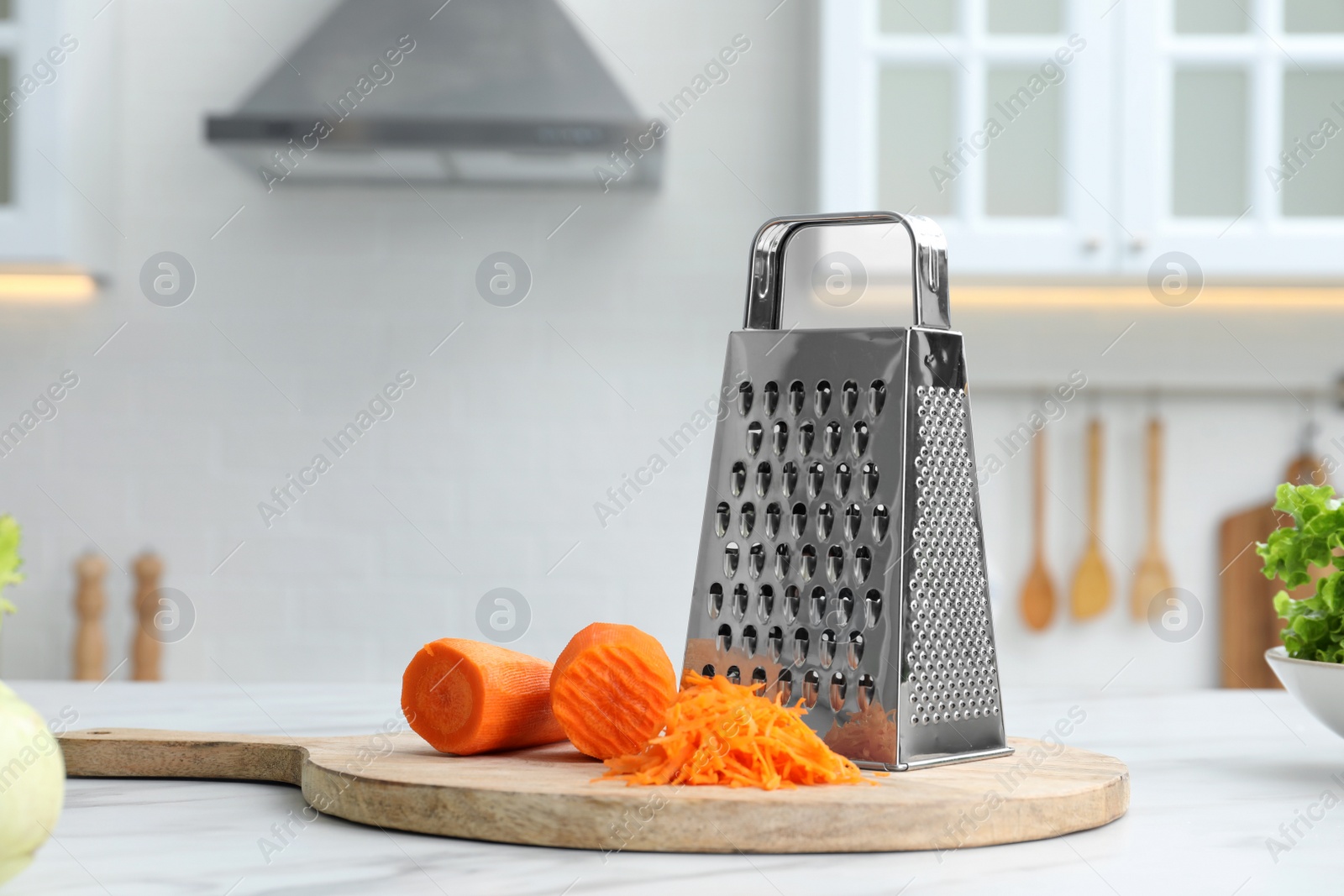 Photo of Grater and fresh ripe carrot on white table in kitchen. Space for text
