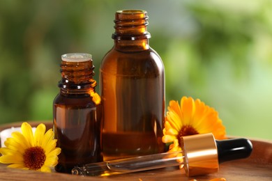 Bottles of essential oils and beautiful calendula flowers on wooden tray outdoors, closeup