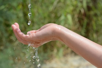 Photo of Pouring water into kid`s hand outdoors, closeup