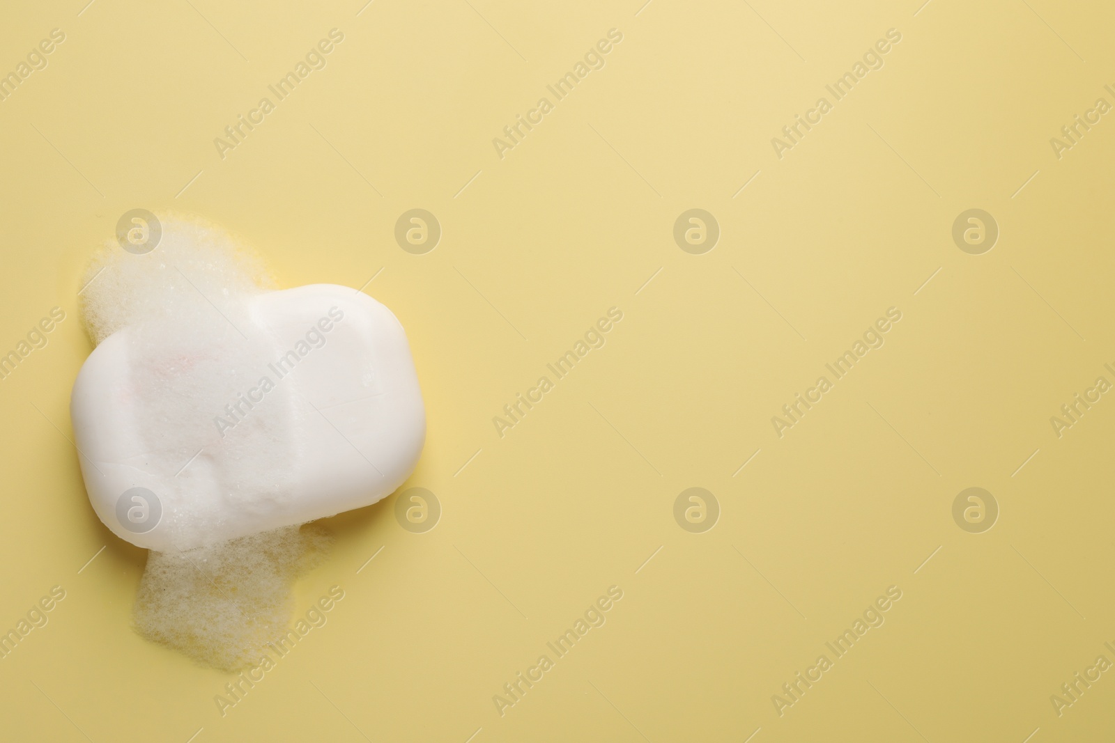Photo of Soap with fluffy foam on yellow background, top view. Space for text