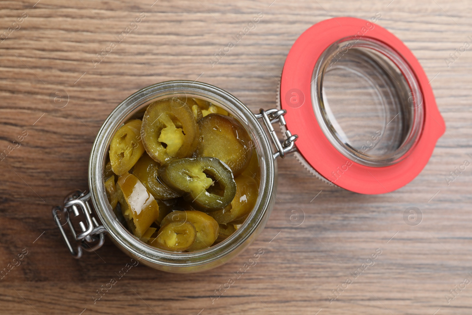 Photo of Glass jar with slices of pickled green jalapeno peppers on wooden table, top view