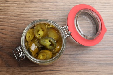 Photo of Glass jar with slices of pickled green jalapeno peppers on wooden table, top view