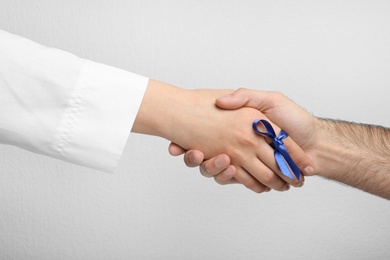 Photo of Doctor with blue ribbon on finger and patient holding hands against grey background, closeup. Symbol of medical issues