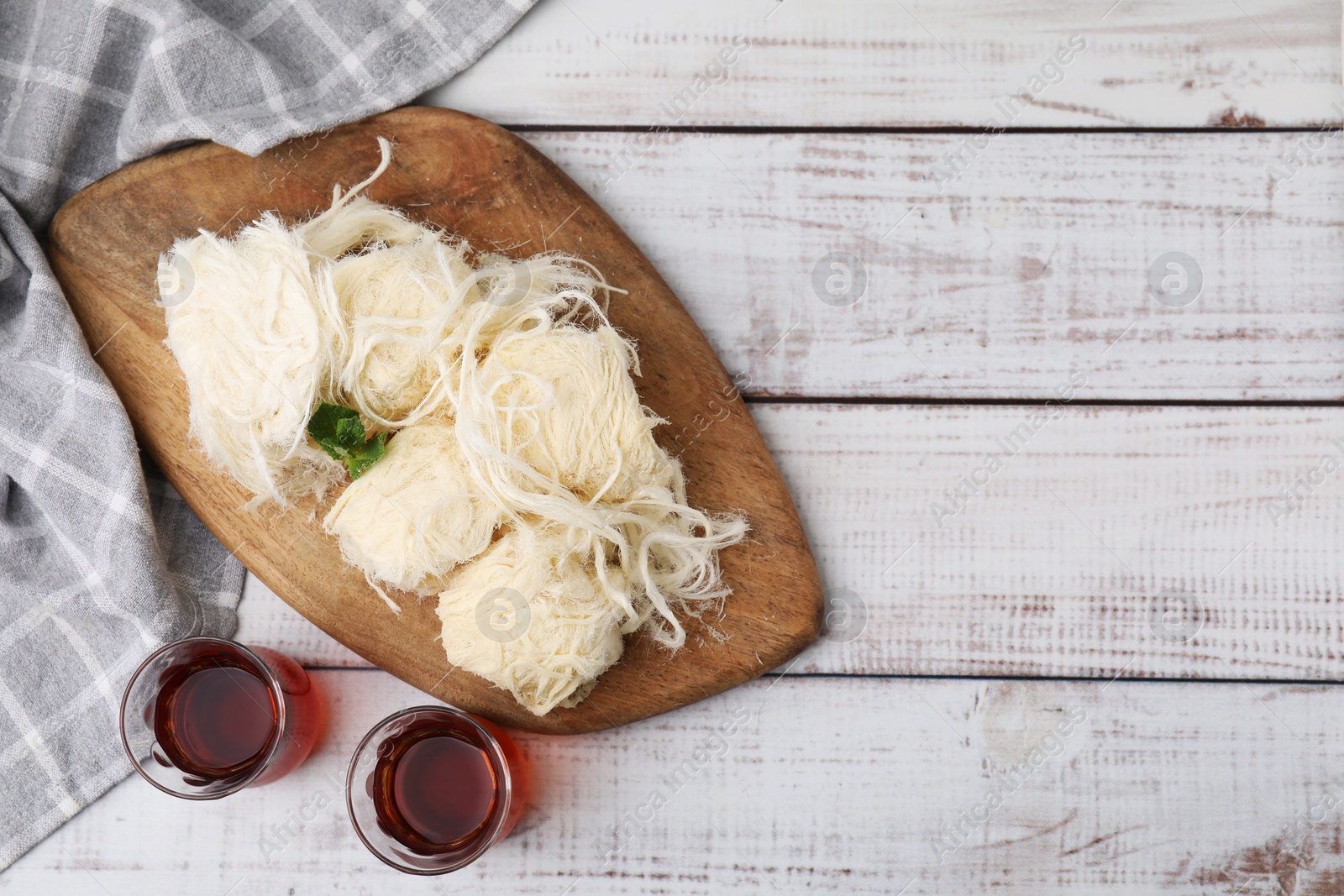 Photo of Eastern sweets. Tasty Iranian pashmak and tea on white wooden table, top view. Space for text