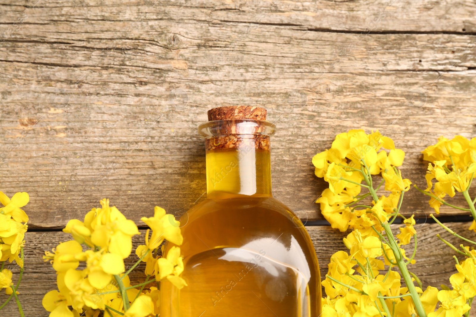 Photo of Rapeseed oil in glass bottle and beautiful yellow flowers on wooden table, flat lay