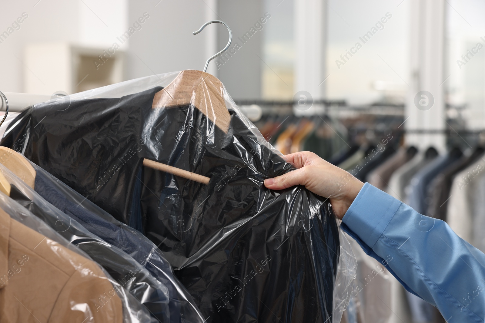 Photo of Dry-cleaning service. Woman taking jacket in plastic bag from rack indoors, closeup