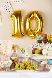 Golden number ten balloon over table with delicious treats at Birthday party indoors