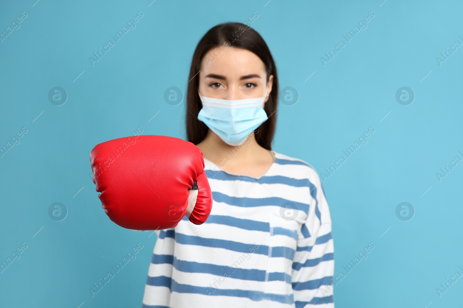 Photo of Woman with protective mask and boxing gloves on light blue background. Strong immunity concept