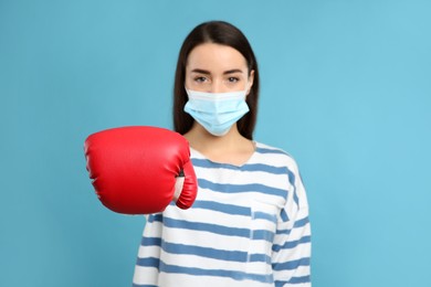 Photo of Woman with protective mask and boxing gloves on light blue background. Strong immunity concept