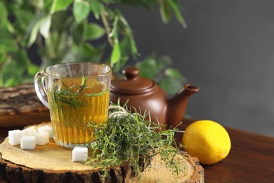 Photo of Aromatic herbal tea, fresh tarragon sprigs and sugar cubes on wooden table. Space for text