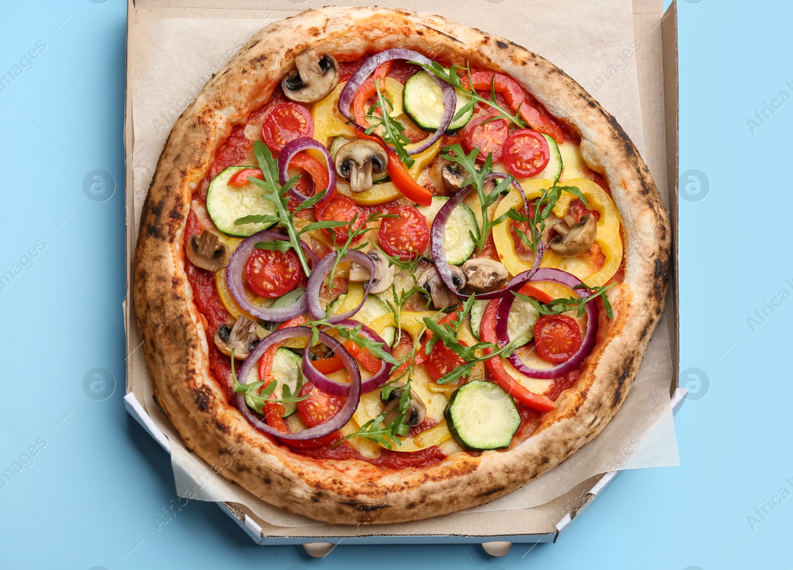 Photo of Delicious vegetable pizza in cardboard box on light blue background, top view