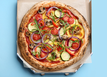 Delicious vegetable pizza in cardboard box on light blue background, top view