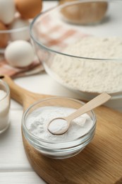 Baking powder in bowl and spoon on white table, closeup