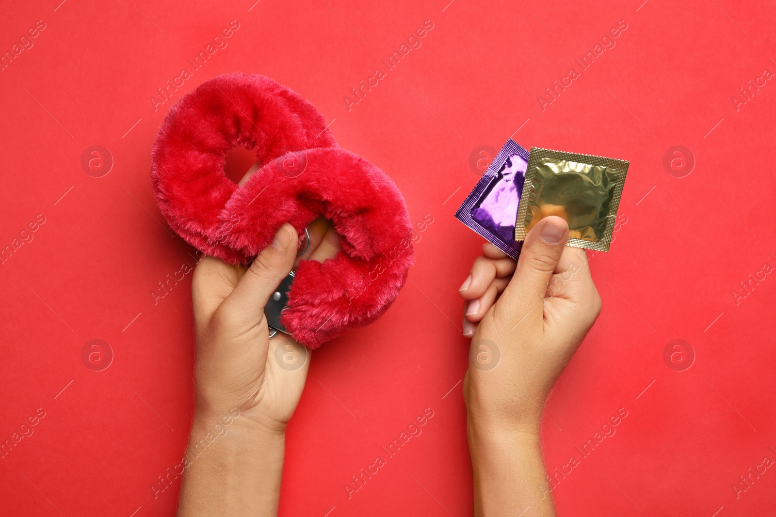 Photo of Woman with furry handcuffs and condoms on red background, top view. Sex game