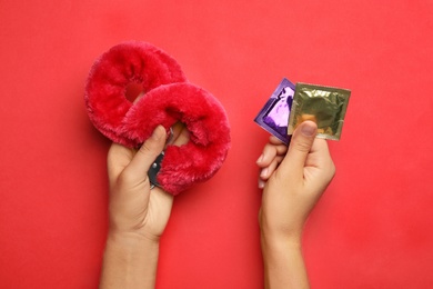 Photo of Woman with furry handcuffs and condoms on red background, top view. Sex game