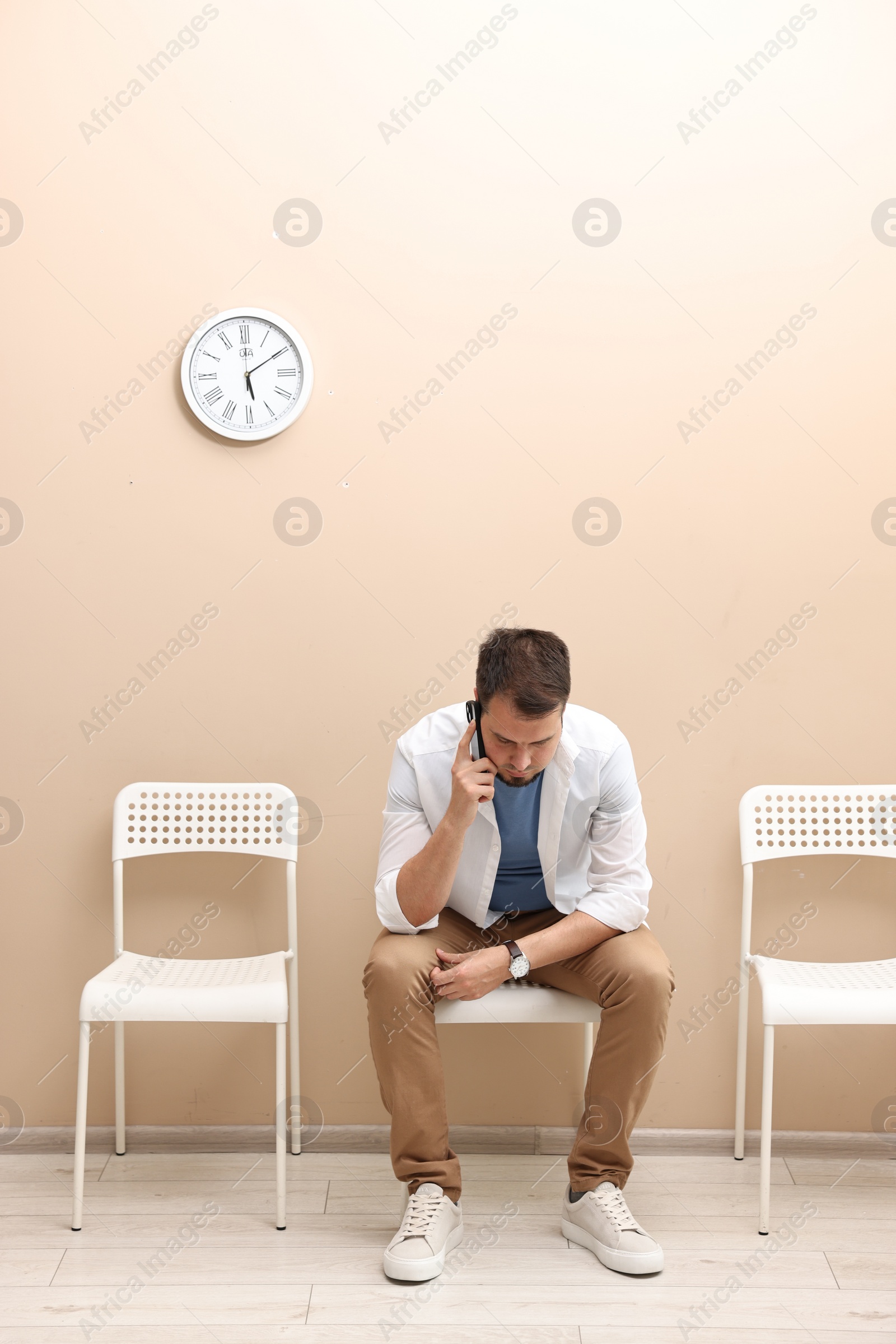 Photo of Man talking on smartphone and waiting for appointment indoors