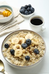 Photo of Tasty oatmeal with banana, blueberries, walnuts and honey served in bowl on white wooden table