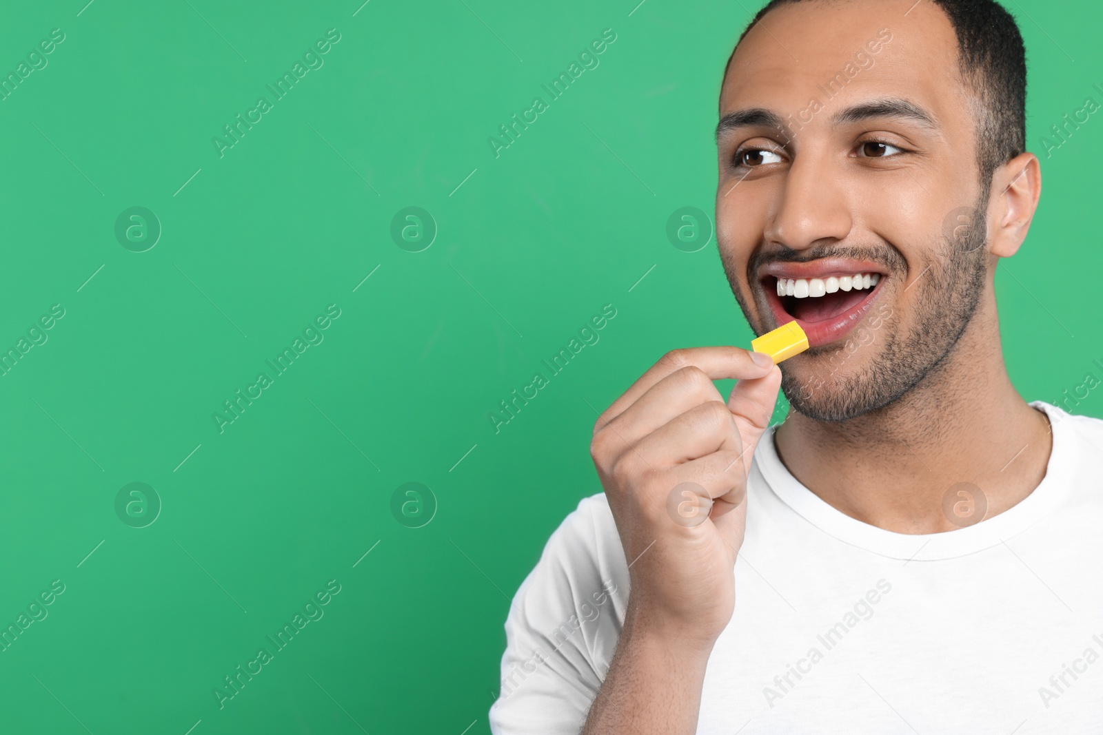 Photo of Happy man putting bubble gum into mouth on green background. Space for text