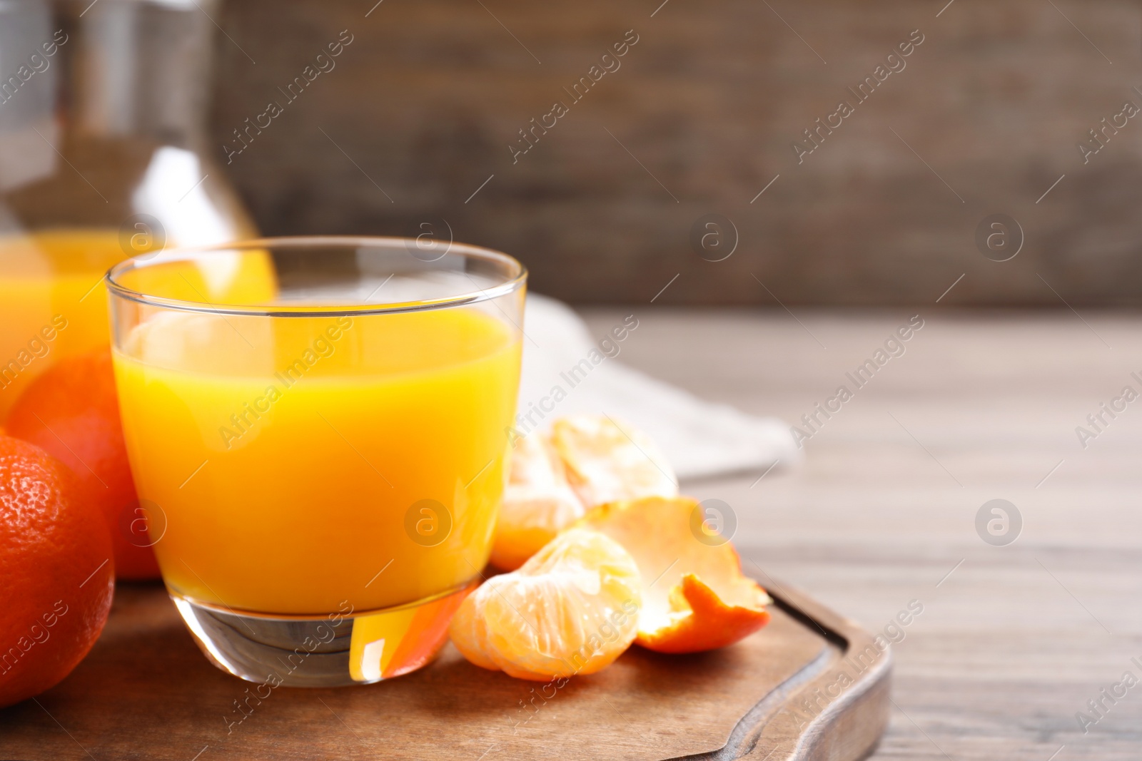 Photo of Glass of fresh tangerine juice and fruits on wooden board, space for text