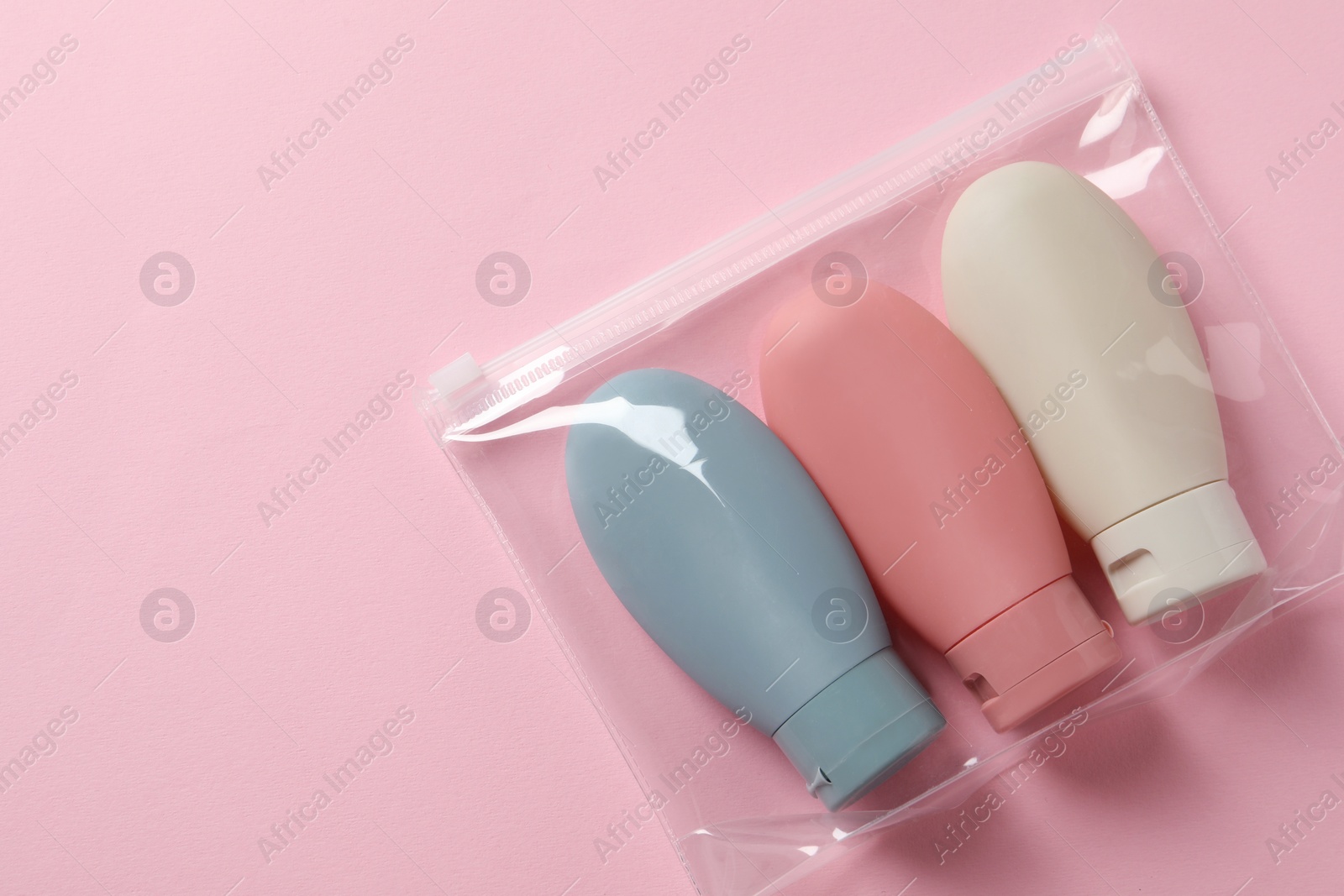 Photo of Cosmetic travel kit in plastic bag on pink background, top view. Space for text