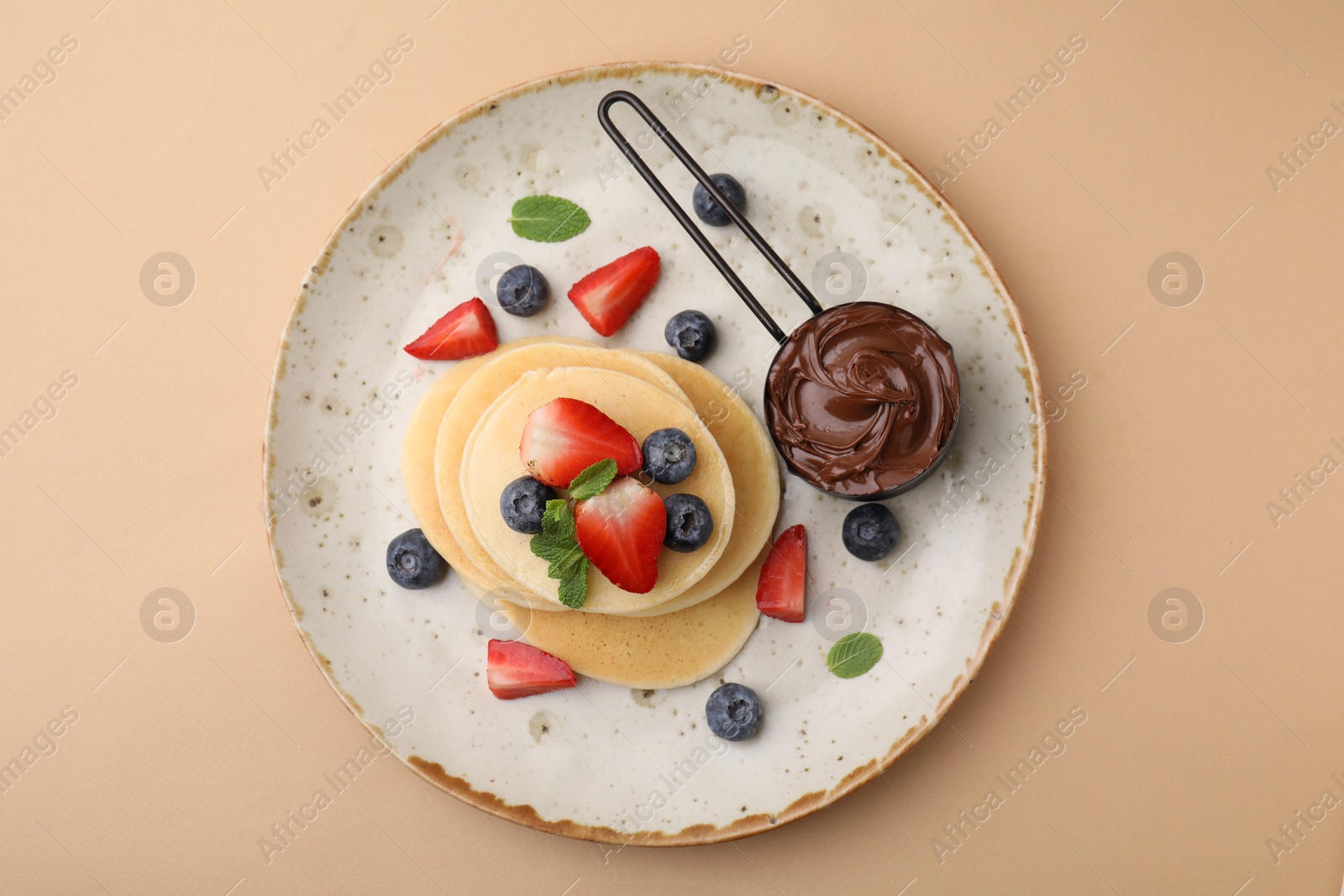 Photo of Delicious pancakes served with berries and chocolate spread on beige background, top view