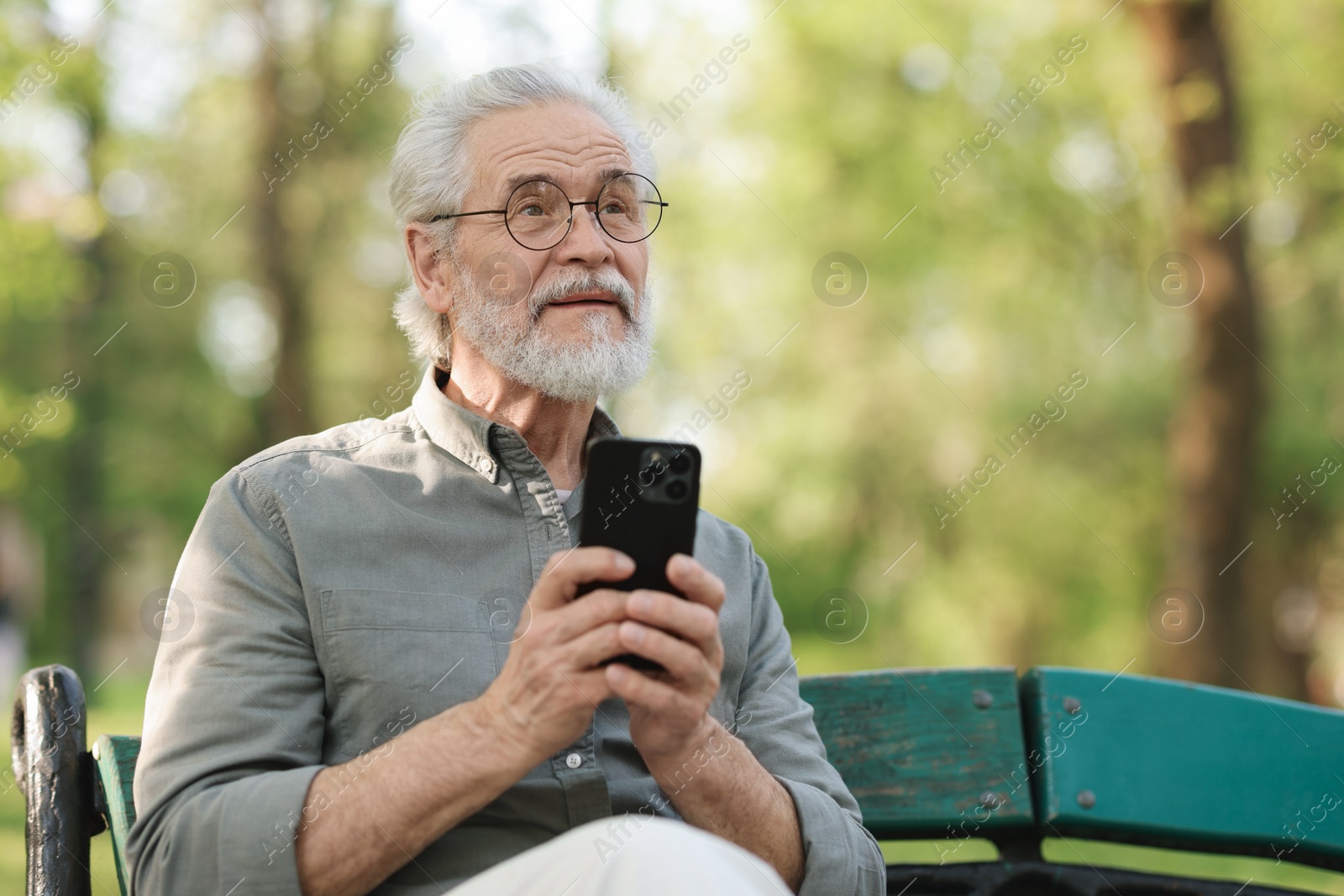 Photo of Portrait of happy grandpa with glasses using smartphone on bench in park