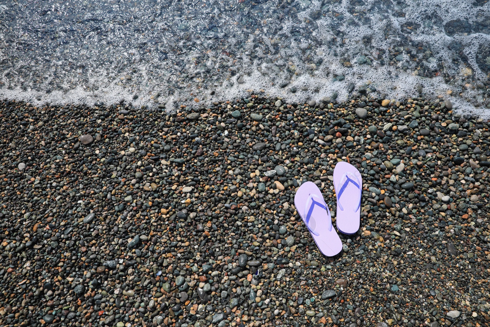 Photo of Stylish lilac flip lops on pebble beach near sea, above view. Space for text