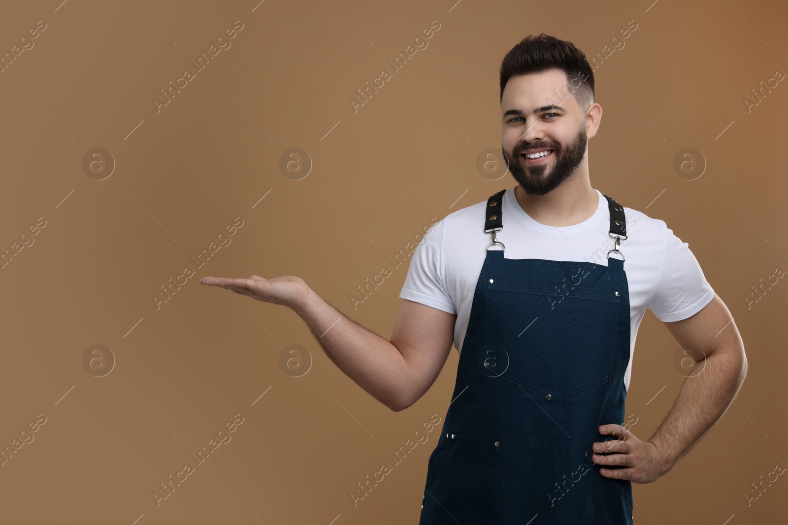 Photo of Smiling man in kitchen apron holding something on brown background. Mockup for design