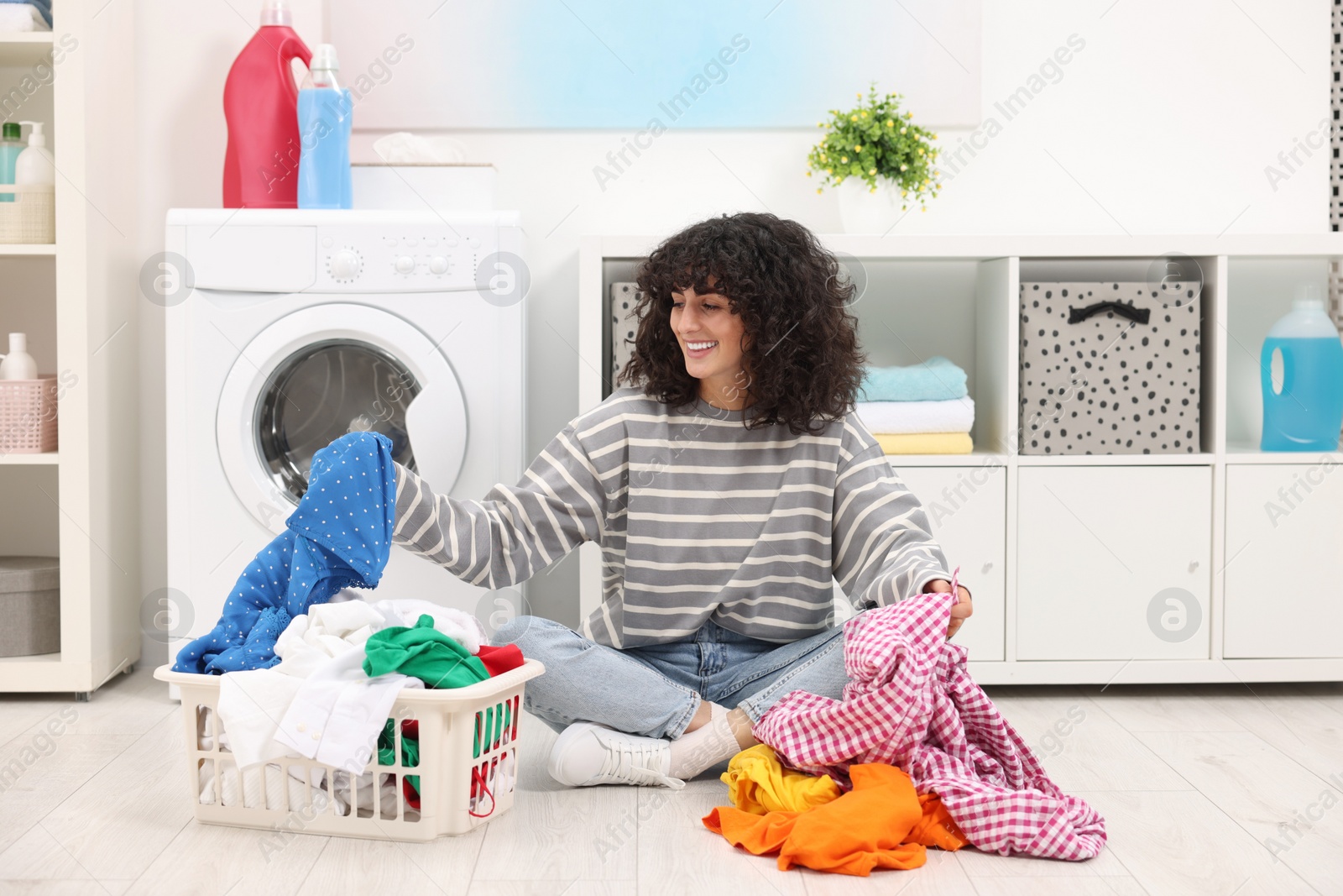 Photo of Happy woman with laundry near washing machine indoors