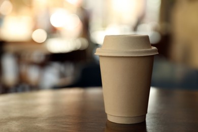 Photo of Cardboard takeaway coffee cup with lid on wooden table in outdoor cafe, space for text