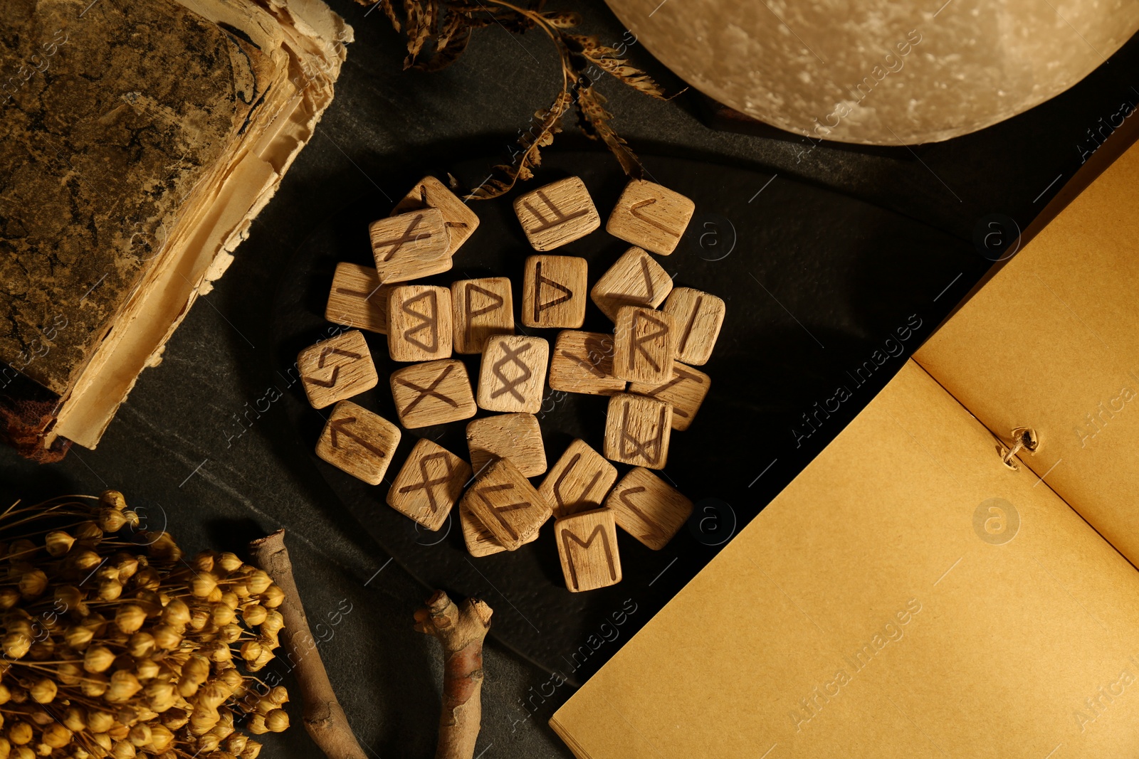 Photo of Wooden runes, dried flowers and old book on black table, flat lay