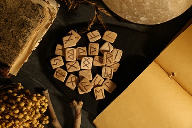 Photo of Wooden runes, dried flowers and old book on black table, flat lay