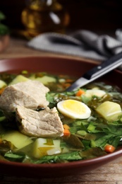 Delicious sorrel soup with meat and egg in brown bowl, closeup
