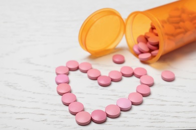 Composition with heart made of pills on white wooden background